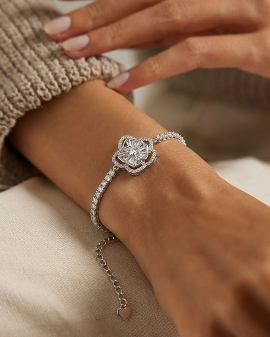 Silver bracelet with a heart charm on a wrist, wearing a beige sweater.