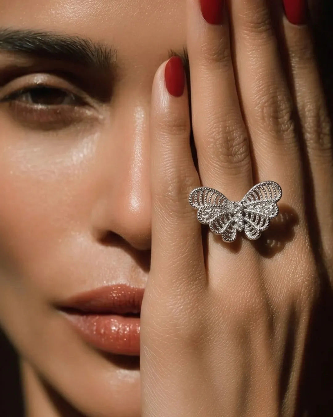 Close-up of a woman's face with a butterfly-shaped ring on her finger.