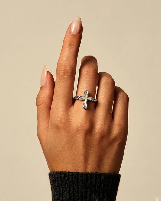 Hand wearing a silver cross ring on a beige background