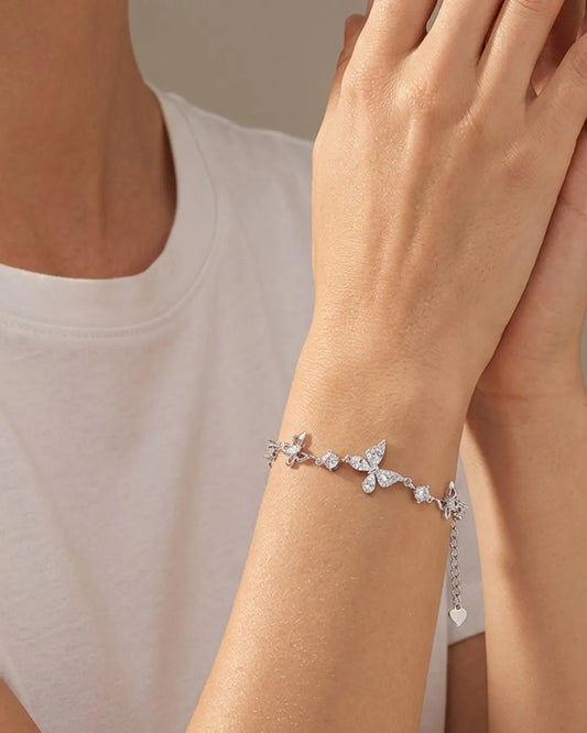 Silver bracelet with butterfly and heart charms on a wrist against a neutral background