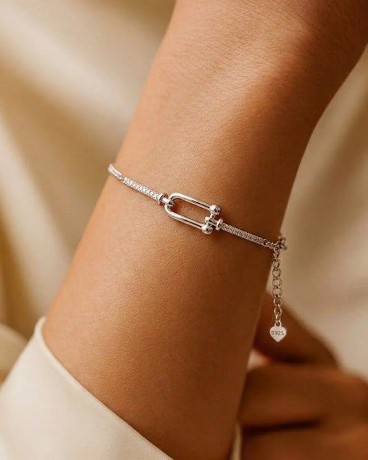 Silver bracelet with a heart charm on a wrist against a beige background