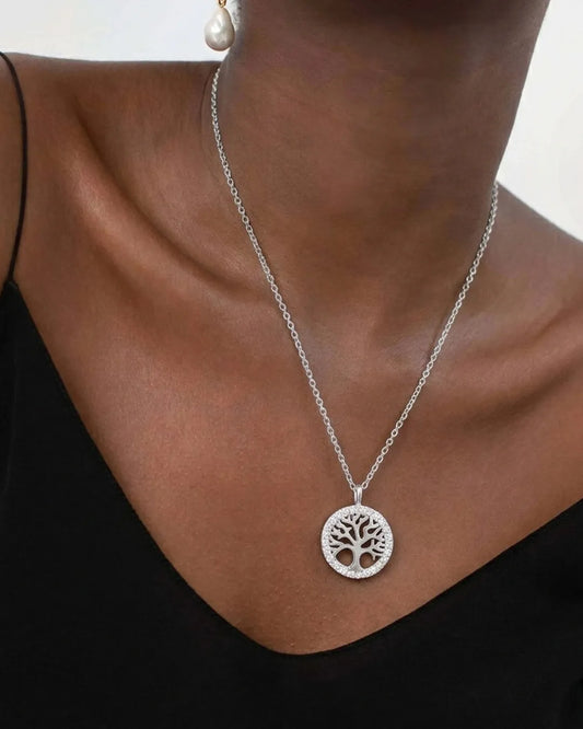 Silver necklace with a tree-of-life pendant worn by a person against a neutral background