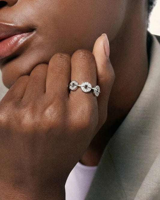 Close-up of a hand wearing a silver ring with a diamond, against a neutral background.