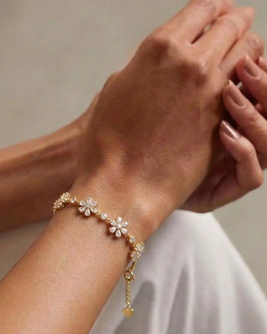 Gold bracelet with floral charms on a wrist against a neutral background