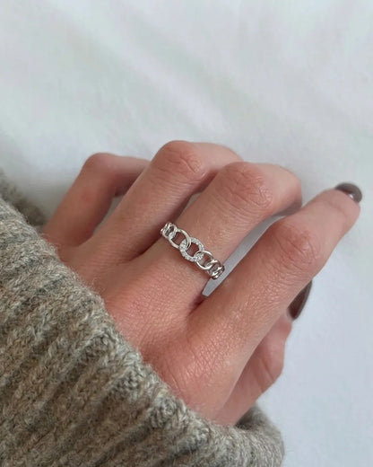 Hand wearing a silver chain ring on a plain background
