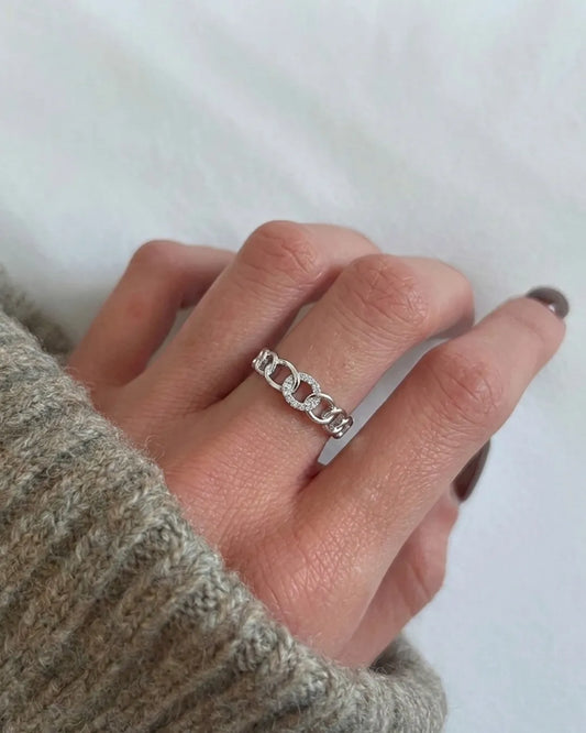Hand wearing a silver chain ring on a plain background