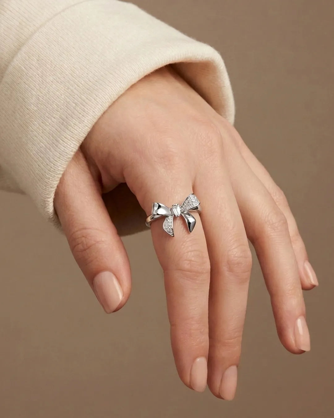 Silver bow-shaped ring on a hand against a beige background