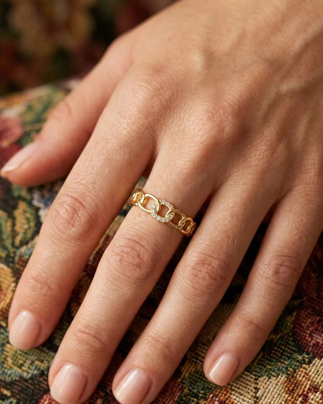 Gold chain ring on a hand with a patterned fabric background