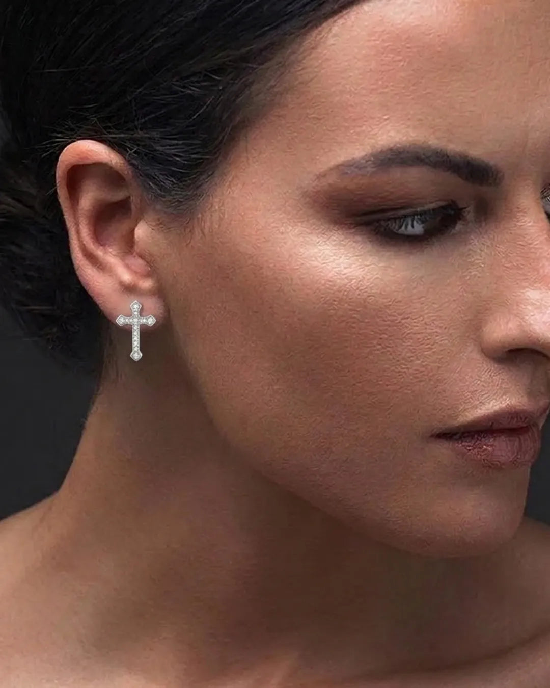 Close-up of a woman wearing a silver cross earring against a dark background