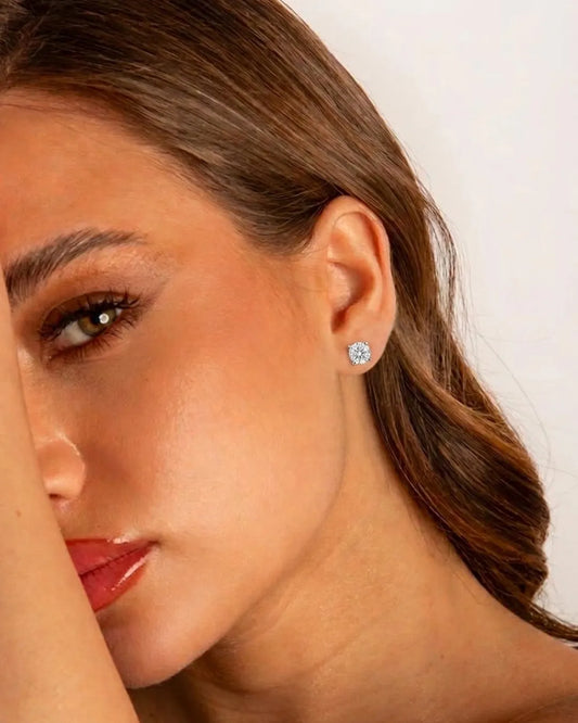 Close-up of a woman wearing diamond stud earrings with a neutral background