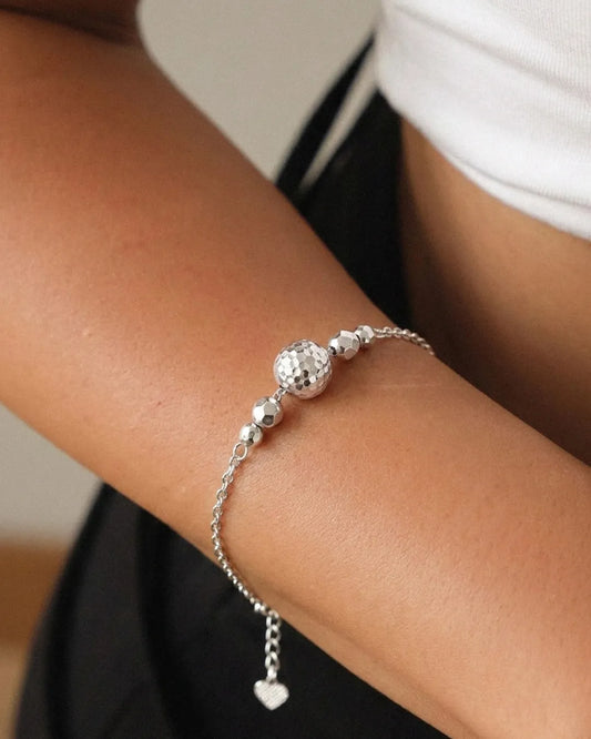 Silver bracelet with heart charm on a wrist against a neutral background