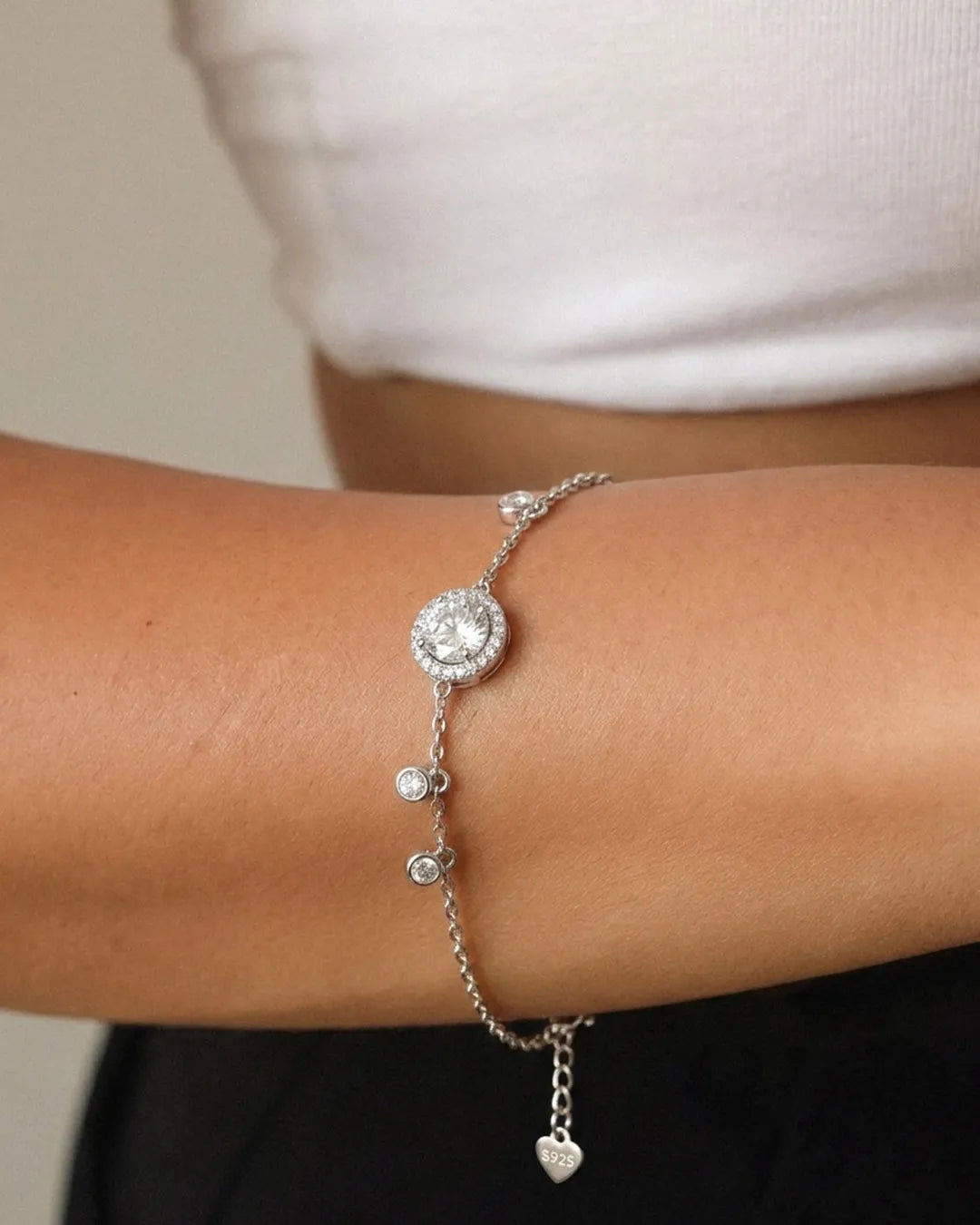Silver bracelet with heart charm on a wrist against a neutral background