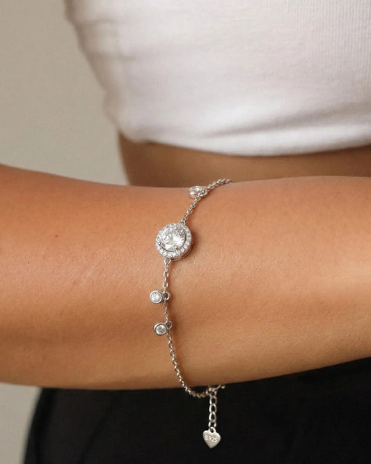 Silver bracelet with heart charm on a wrist against a neutral background