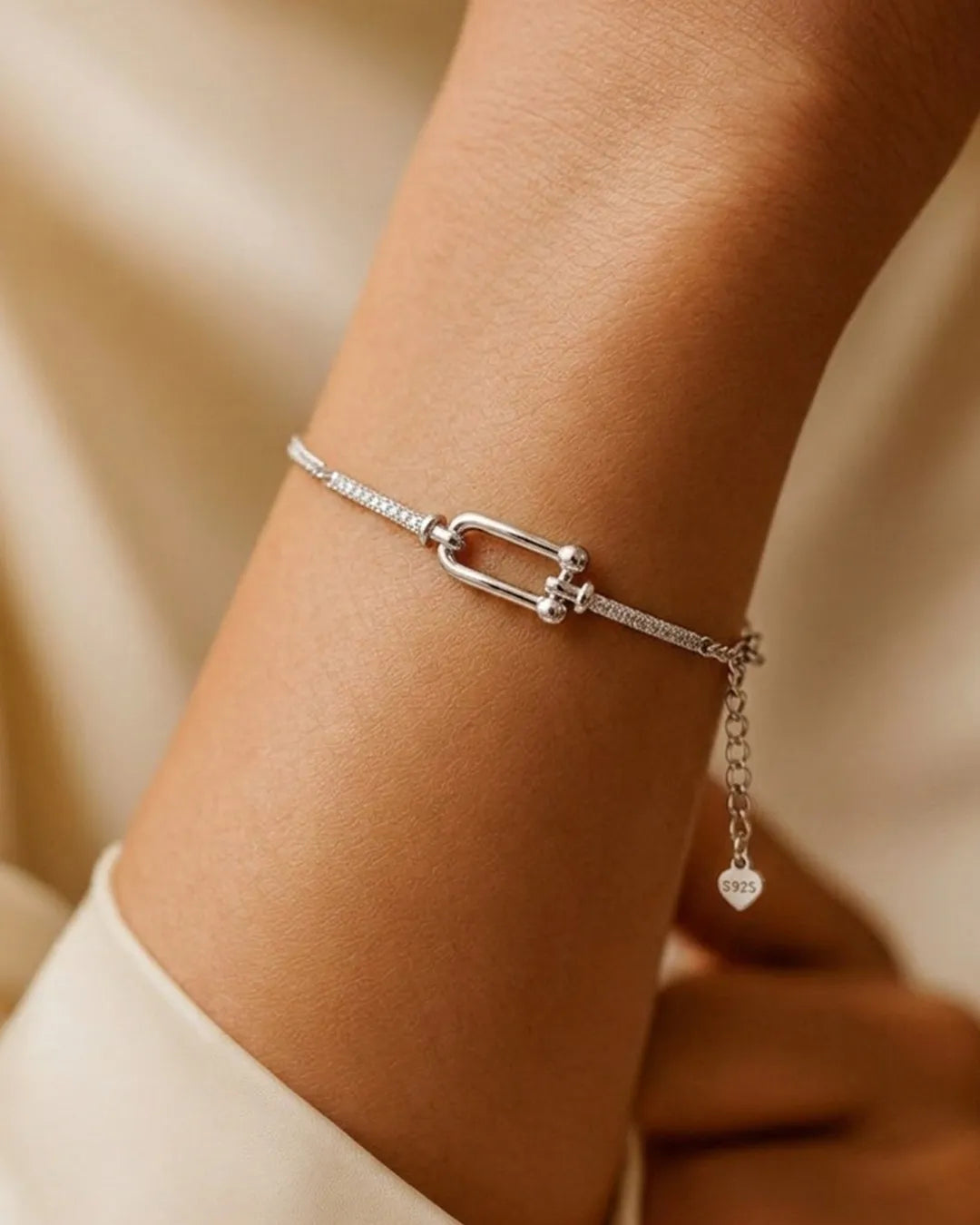 Silver bracelet with a heart charm on a wrist against a beige background