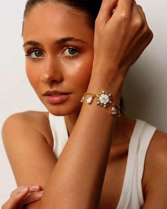 Woman wearing a gold bracelet with a large central stone and smaller stones on a plain background